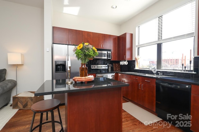 kitchen featuring reddish brown cabinets, a center island, a breakfast bar, backsplash, and appliances with stainless steel finishes