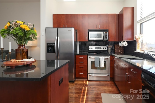 kitchen with stainless steel appliances, a sink, dark brown cabinets, backsplash, and dark stone countertops