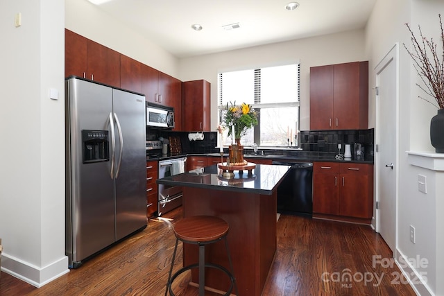 kitchen with a center island, dark wood-style flooring, stainless steel appliances, dark countertops, and tasteful backsplash