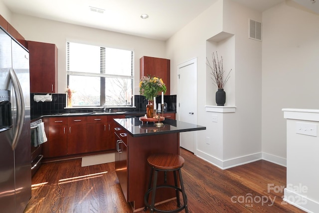 kitchen featuring dark wood-style flooring, a sink, a kitchen island, visible vents, and stainless steel fridge with ice dispenser