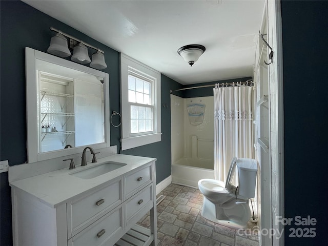 bathroom with toilet, shower / bath combo with shower curtain, stone finish floor, vanity, and baseboards