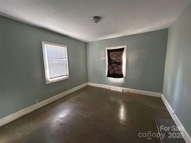 spare room featuring dark wood-style floors, visible vents, and baseboards