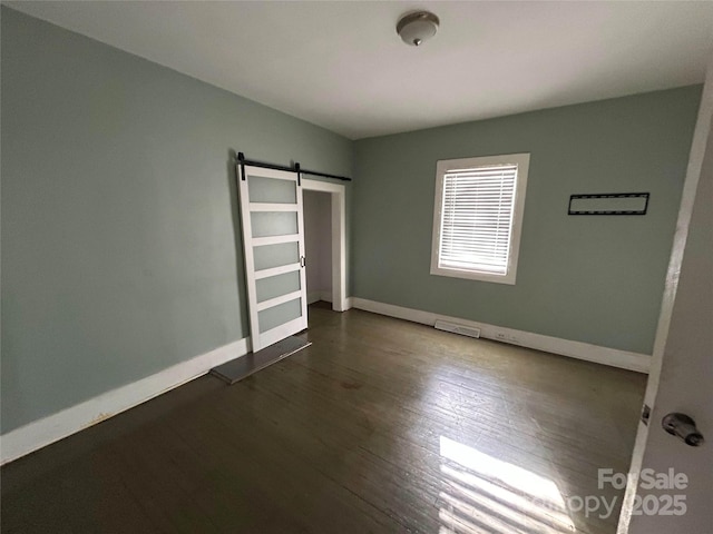 unfurnished bedroom featuring dark wood-style floors, visible vents, baseboards, and a barn door