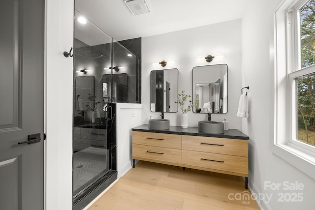 bathroom featuring visible vents, a shower stall, double vanity, wood finished floors, and a sink