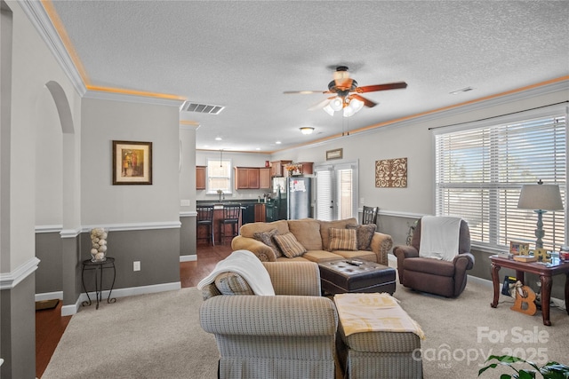 carpeted living room featuring arched walkways, visible vents, ceiling fan, a textured ceiling, and baseboards