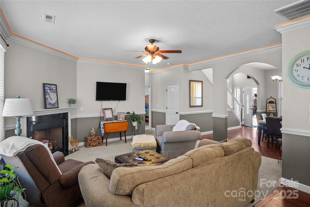 living room featuring arched walkways, a fireplace, visible vents, and crown molding