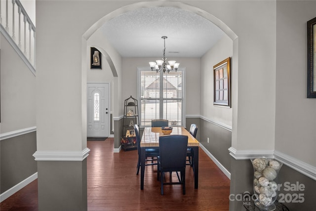 dining space with a textured ceiling, dark wood-type flooring, baseboards, and a notable chandelier