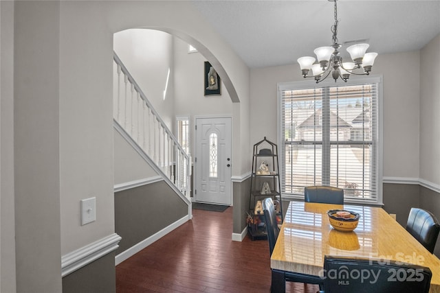 dining area featuring baseboards, dark wood finished floors, arched walkways, an inviting chandelier, and stairs