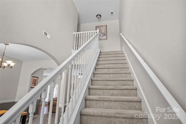 stairway with arched walkways, visible vents, a high ceiling, and an inviting chandelier