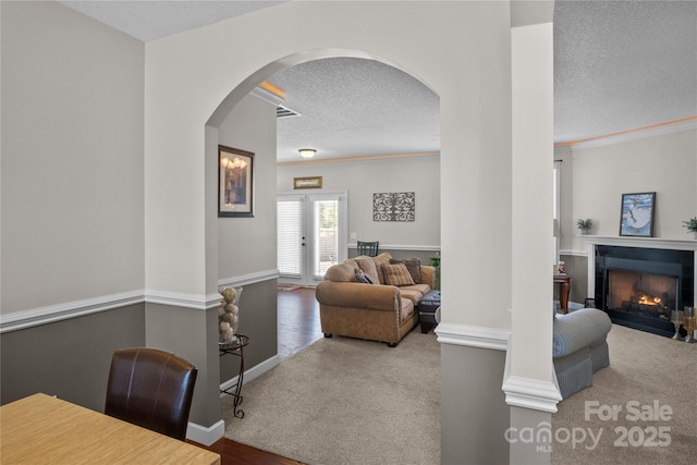 living room featuring carpet, crown molding, visible vents, a fireplace with flush hearth, and a textured ceiling