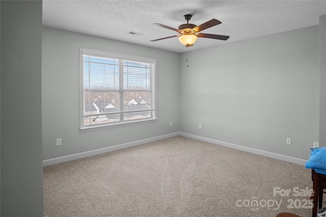 spare room with carpet floors, visible vents, a textured ceiling, and baseboards