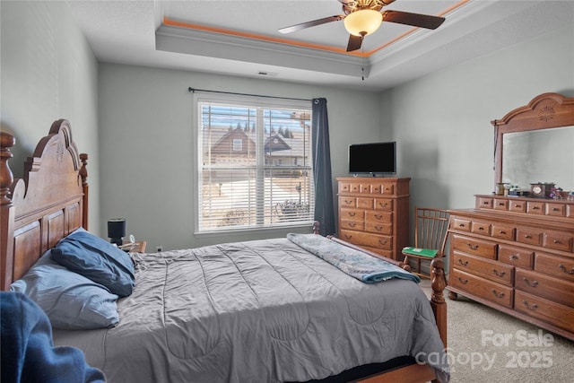 carpeted bedroom with a tray ceiling, crown molding, and ceiling fan