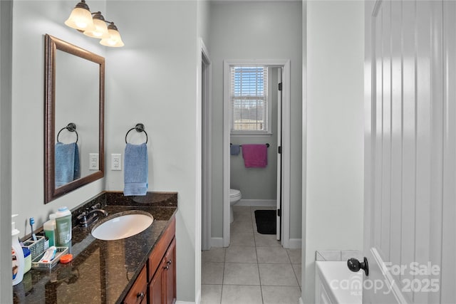 bathroom featuring toilet, vanity, a tub, baseboards, and tile patterned floors