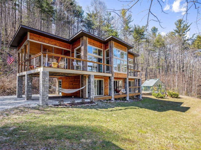 back of house with a lawn, a patio, stone siding, an outbuilding, and an exterior structure