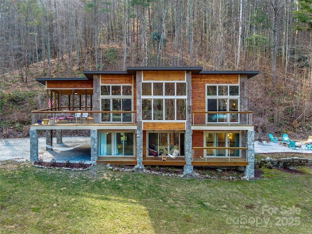 rear view of property featuring a balcony, a patio area, a wooded view, and a yard