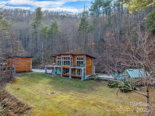 rear view of house featuring a lawn, an outdoor structure, and a view of trees