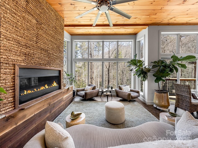 living area featuring a glass covered fireplace, wooden ceiling, ceiling fan, and a towering ceiling