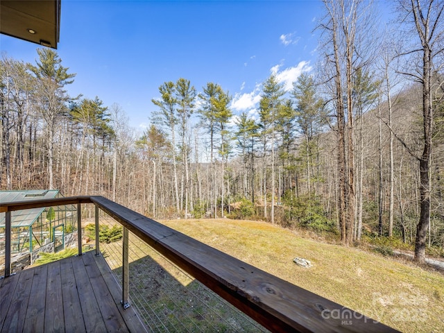 wooden terrace with a lawn and a view of trees