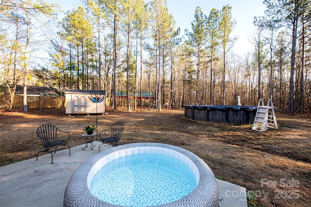 view of pool with an outbuilding, fence, a covered pool, a storage unit, and a patio area