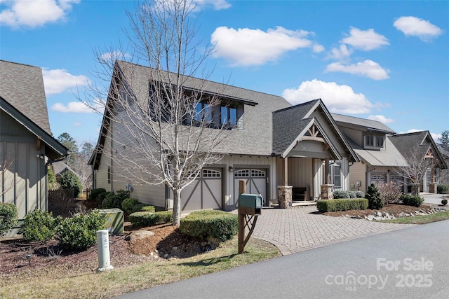 view of front facade featuring board and batten siding, a garage, decorative driveway, and roof with shingles