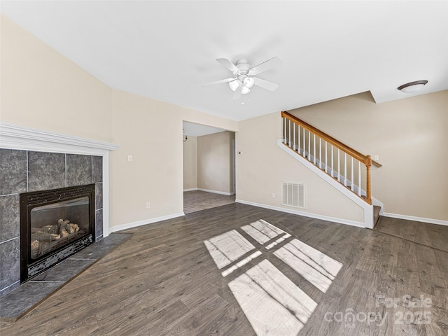 unfurnished living room featuring a fireplace, visible vents, baseboards, stairway, and dark wood-style floors