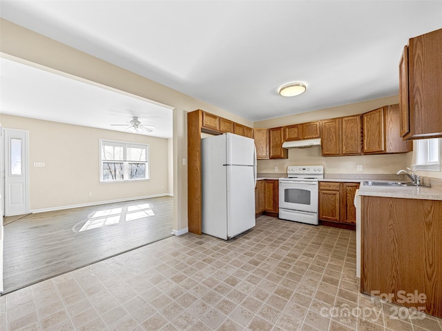 kitchen with light countertops, brown cabinetry, a sink, white appliances, and under cabinet range hood