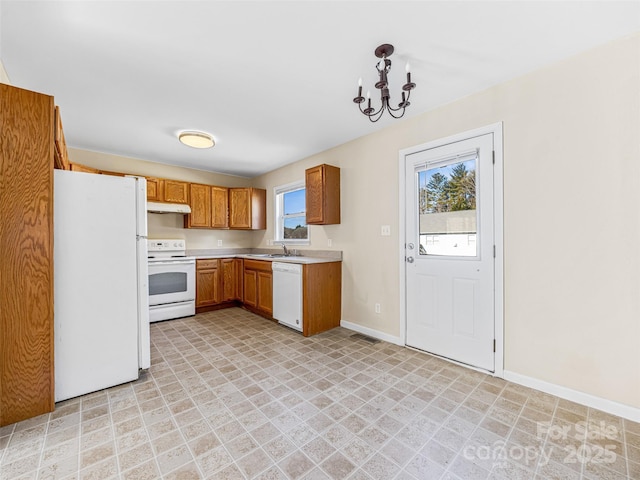 kitchen featuring white appliances, brown cabinets, light countertops, under cabinet range hood, and a sink