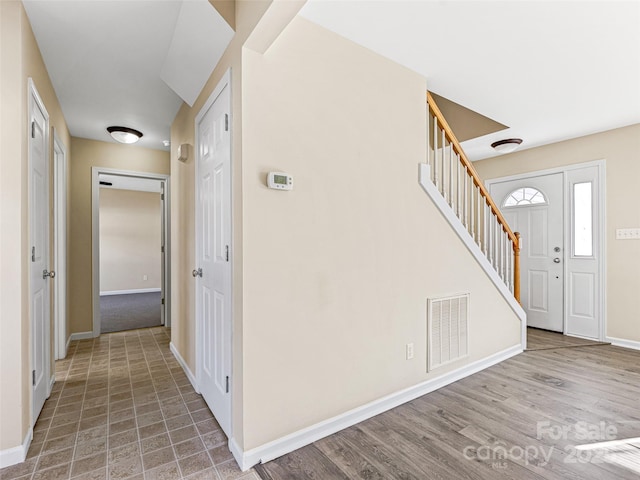 foyer featuring baseboards, stairs, visible vents, and wood finished floors