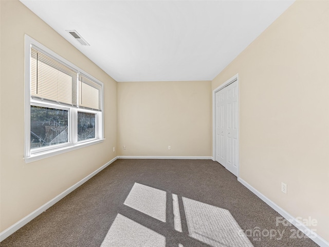 empty room with baseboards, visible vents, and dark carpet