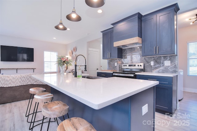 kitchen featuring open floor plan, light countertops, a center island with sink, and stainless steel range with electric cooktop