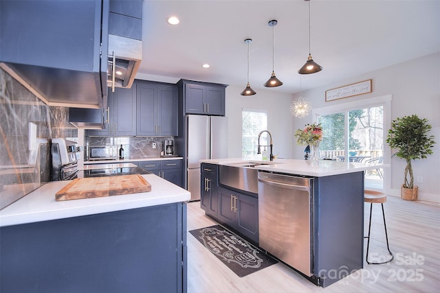 kitchen featuring light countertops, appliances with stainless steel finishes, an island with sink, and decorative light fixtures