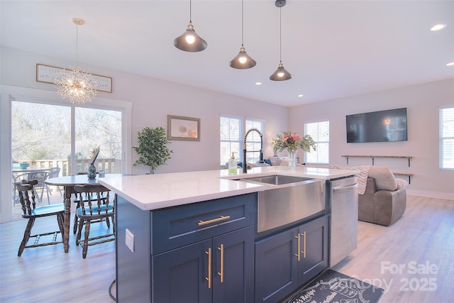 kitchen with open floor plan, light countertops, stainless steel dishwasher, an island with sink, and pendant lighting