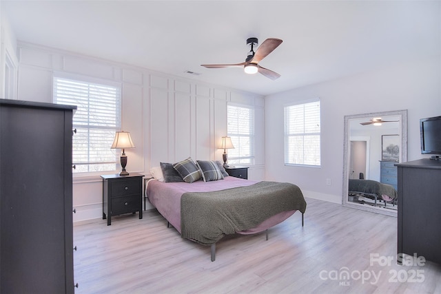 bedroom featuring light wood-style floors, visible vents, a decorative wall, and multiple windows