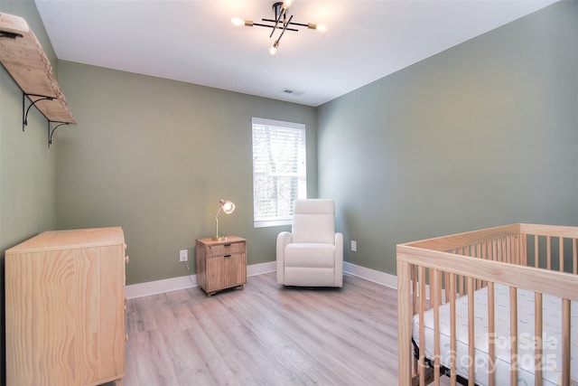 bedroom featuring a crib, light wood finished floors, visible vents, baseboards, and an inviting chandelier