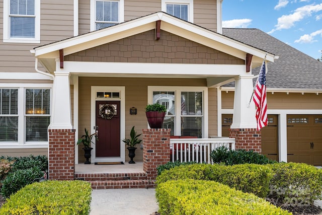 entrance to property featuring a porch, roof with shingles, an attached garage, and brick siding