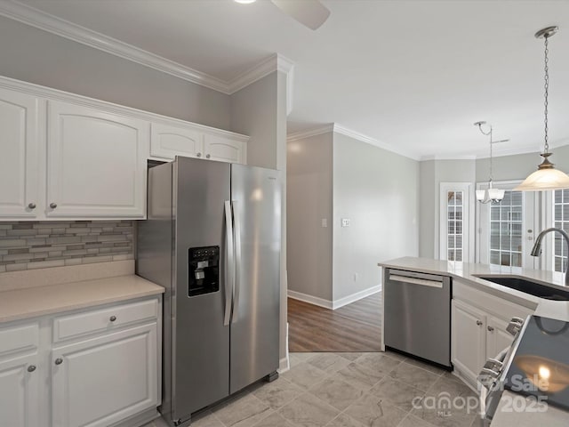 kitchen with stainless steel appliances, light countertops, ornamental molding, white cabinets, and a sink