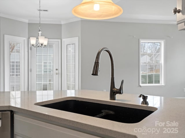 kitchen featuring hanging light fixtures, light stone counters, a sink, and crown molding