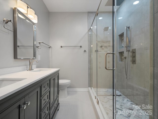 bathroom with double vanity, a stall shower, baseboards, toilet, and a sink