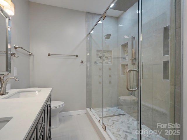 bathroom featuring toilet, a shower stall, baseboards, and vanity