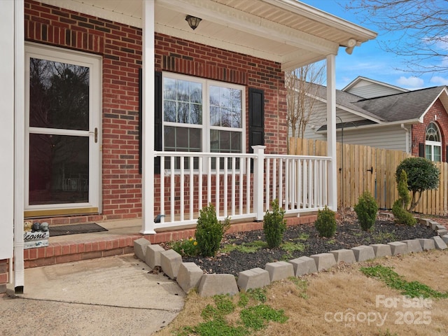 doorway to property with a porch, brick siding, and fence