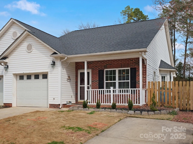 view of front of house featuring a shingled roof, concrete driveway, an attached garage, covered porch, and fence