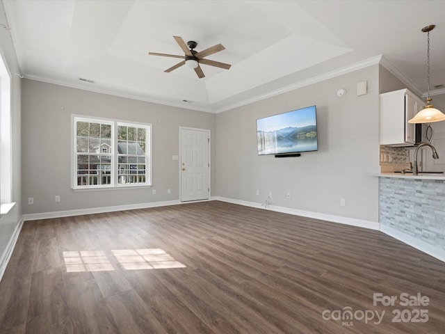 unfurnished living room with crown molding, baseboards, a raised ceiling, and dark wood finished floors