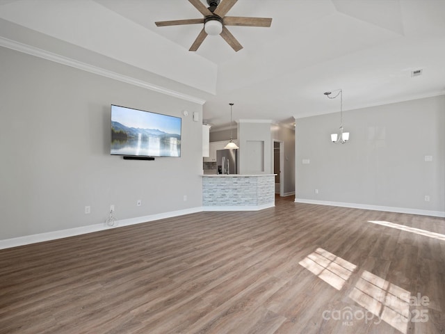 unfurnished living room with ceiling fan with notable chandelier, crown molding, wood finished floors, and baseboards