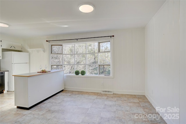 kitchen with light countertops, visible vents, freestanding refrigerator, white cabinetry, and a peninsula