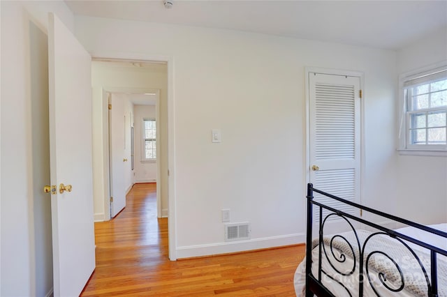 corridor with light wood-style floors, a healthy amount of sunlight, visible vents, and baseboards