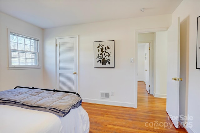 bedroom with a closet, light wood-type flooring, visible vents, and baseboards