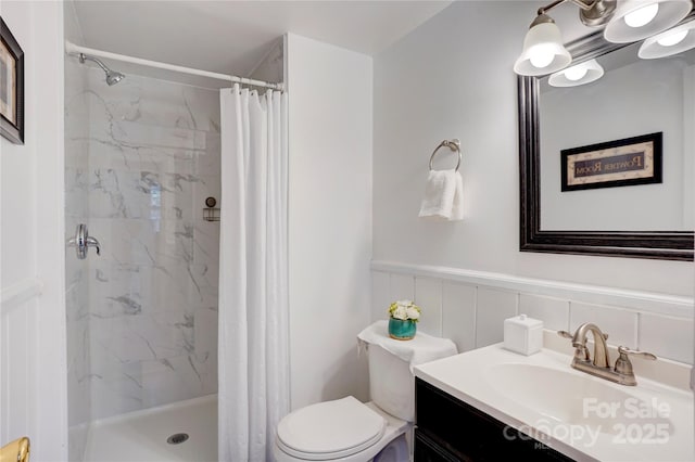 full bath featuring wainscoting, toilet, vanity, and a marble finish shower