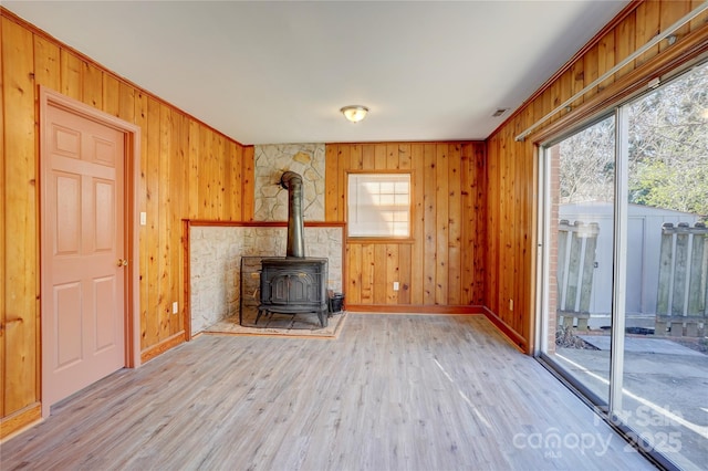 unfurnished living room featuring a wood stove, light wood finished floors, and a wealth of natural light