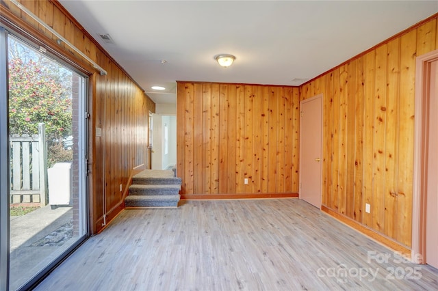 unfurnished room with light wood-style floors, visible vents, wood walls, and stairway