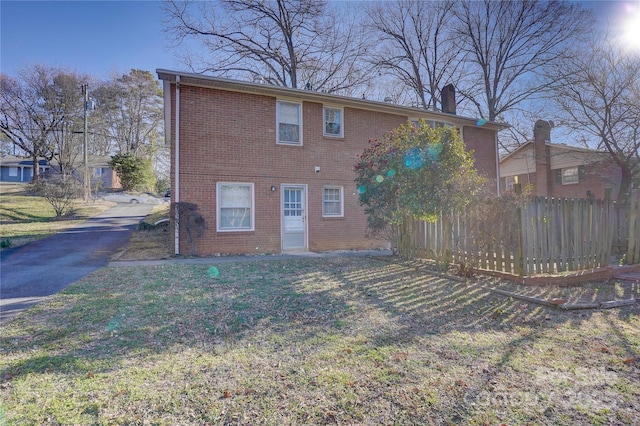 rear view of house with brick siding, a lawn, a chimney, and fence